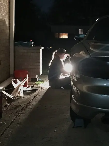 Nikki putting the wheel back onto her 2000 Pontiac Firebird after replacing the sway bar in her driveway. She learned all of her driveway work from independent study, as she had no experienced mechanics in the family to teach her. 